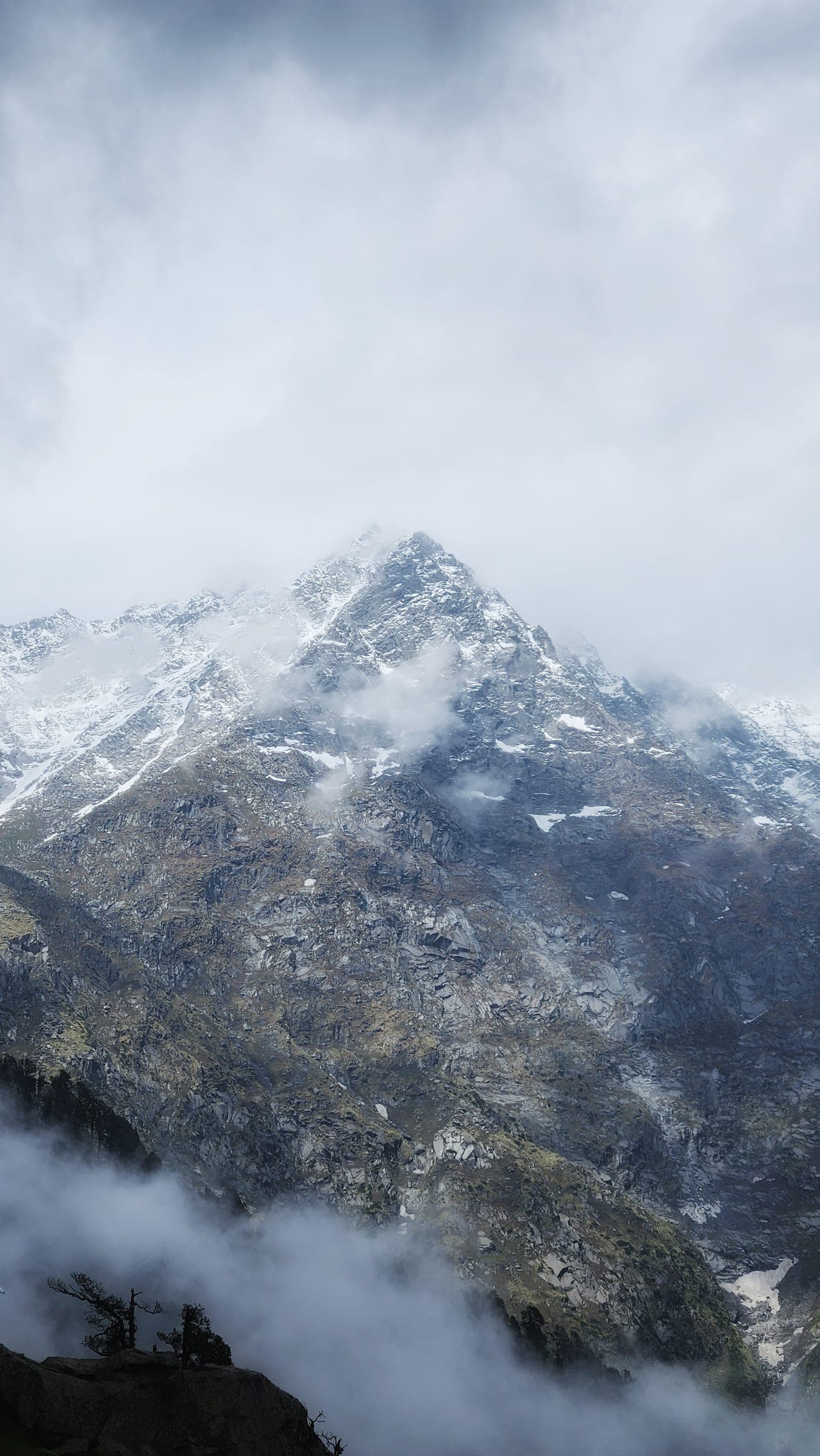 A sharp snow-dusted peak going in and out of cloud, its lower slopes bare rock.