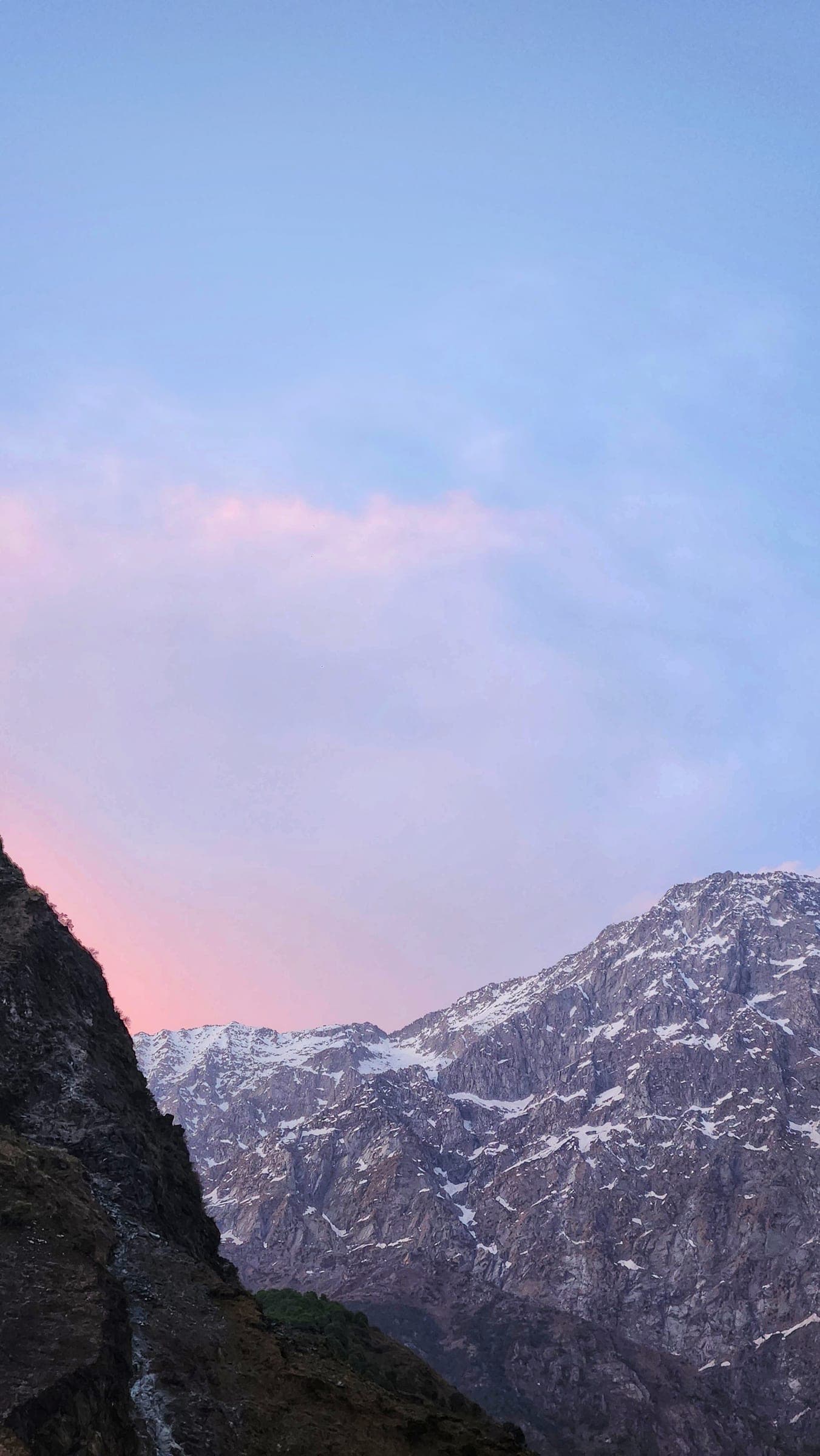 Pink and blue twilight over a snow-covered ridge, a dark cliff cutting into the frame from the left.