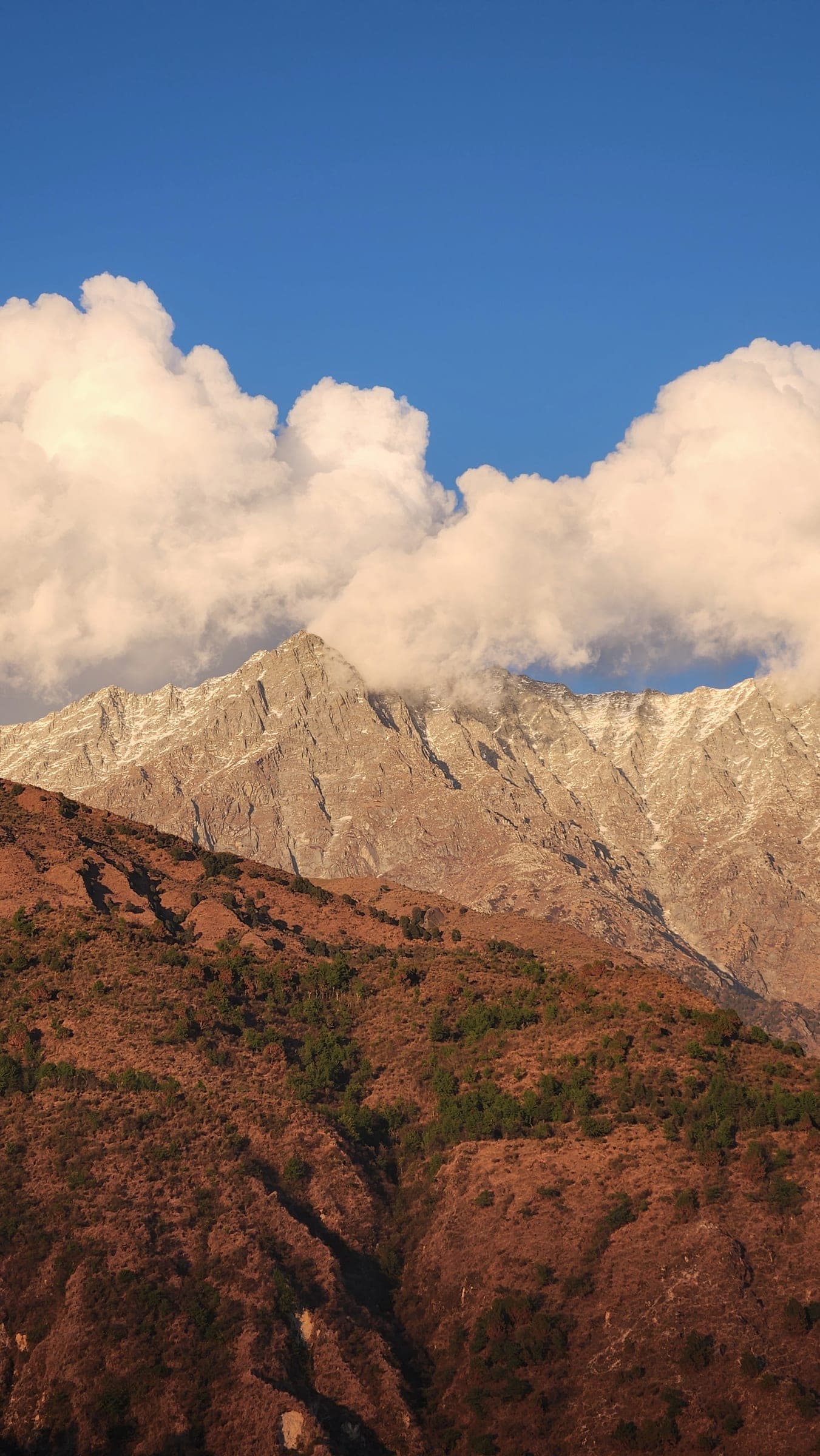 Cumulus piled on a snow-lit ridge, the red-brown hillside below it in late afternoon sun.